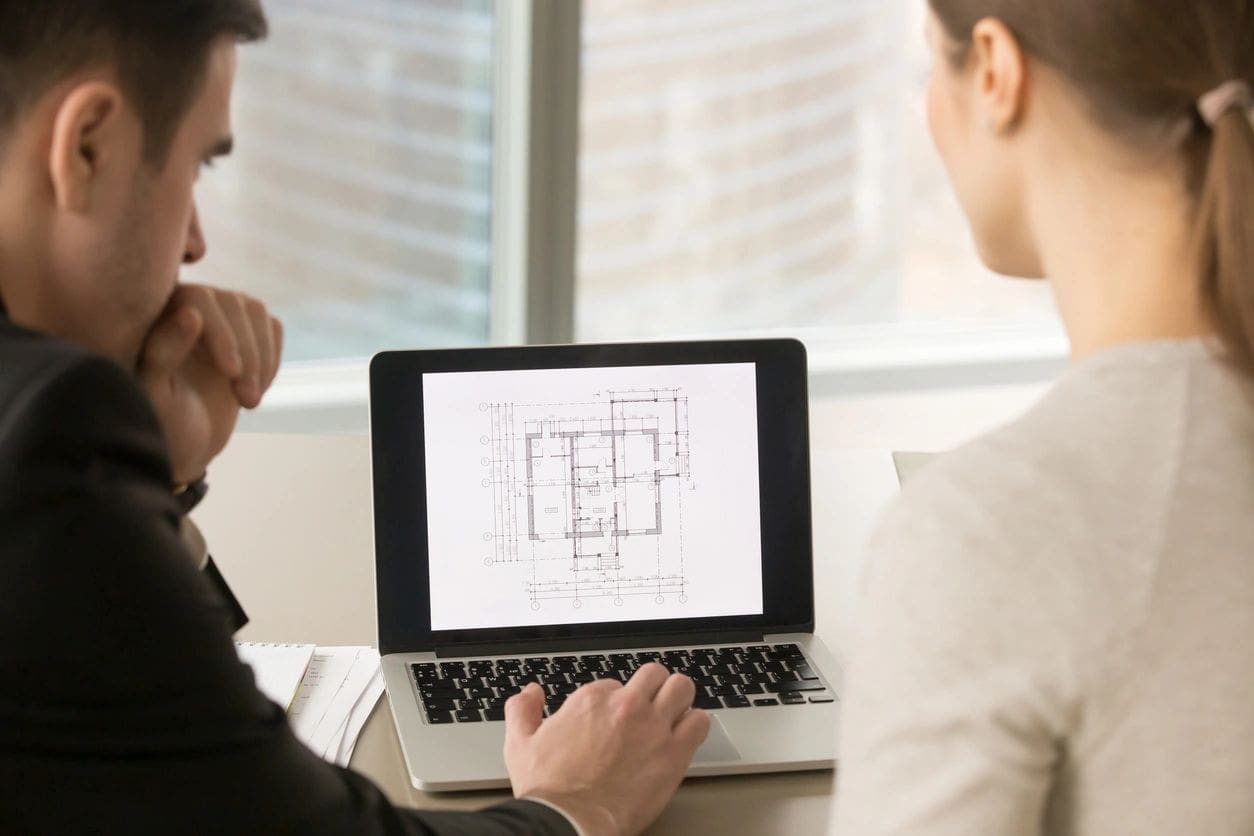 Two people reviewing building plans on laptop.
